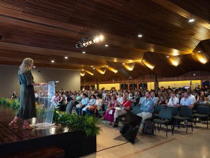 A woman behind a podium delivers a presentation to a large audience